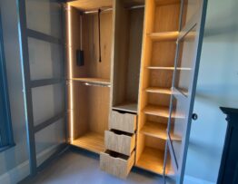 Illuminated fitted wardrobe interior with oak shelving and painted framed glass doors